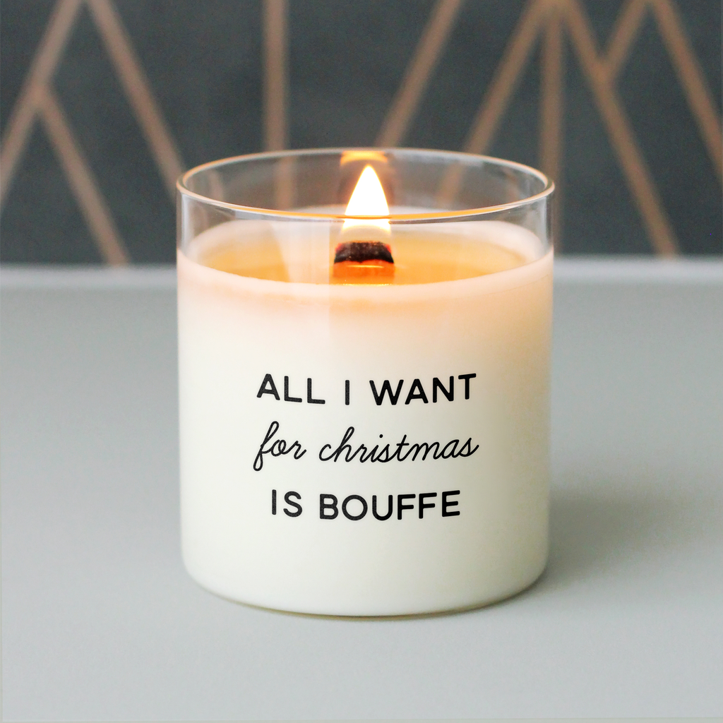 Bougie de Noël humoristique avec le message "All I want for Christmas is bouffe", allumée sur fond géométrique noir et or, parfaite pour un cadeau drôle et gourmand à offrir pendant les fêtes.
