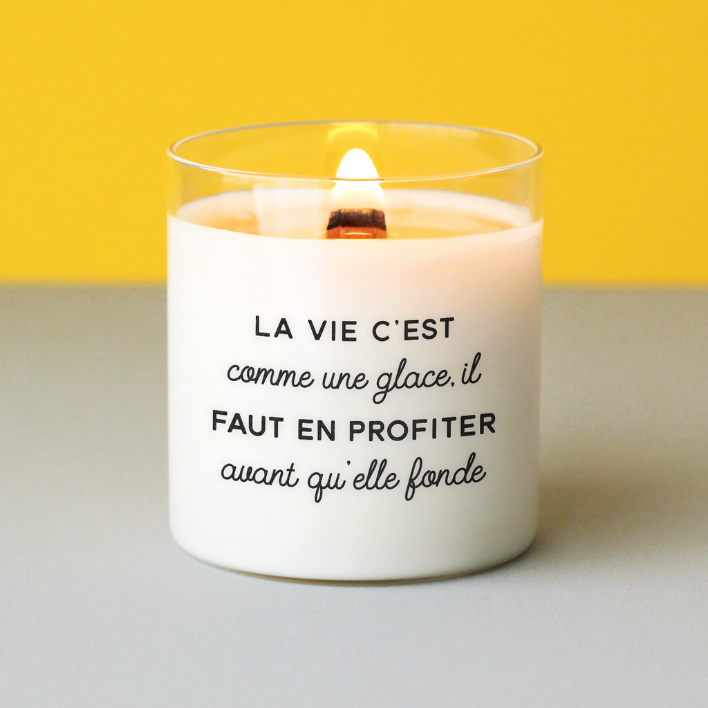 Bougie allumée portant le message "La vie c’est comme une glace, il faut en profiter avant qu’elle fonde", posée sur une table avec fond jaune, idéale comme idée cadeau positive et gourmande.