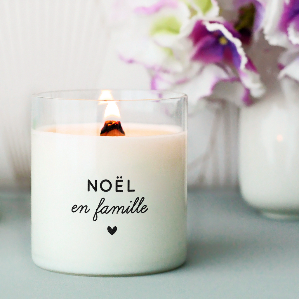 Bougie blanche avec le message « Noël en famille » suivi d’un petit cœur noir, imprimée sur une étiquette transparente sur un contenant en verre. Parfaite pour créer une ambiance chaleureuse pendant les fêtes.