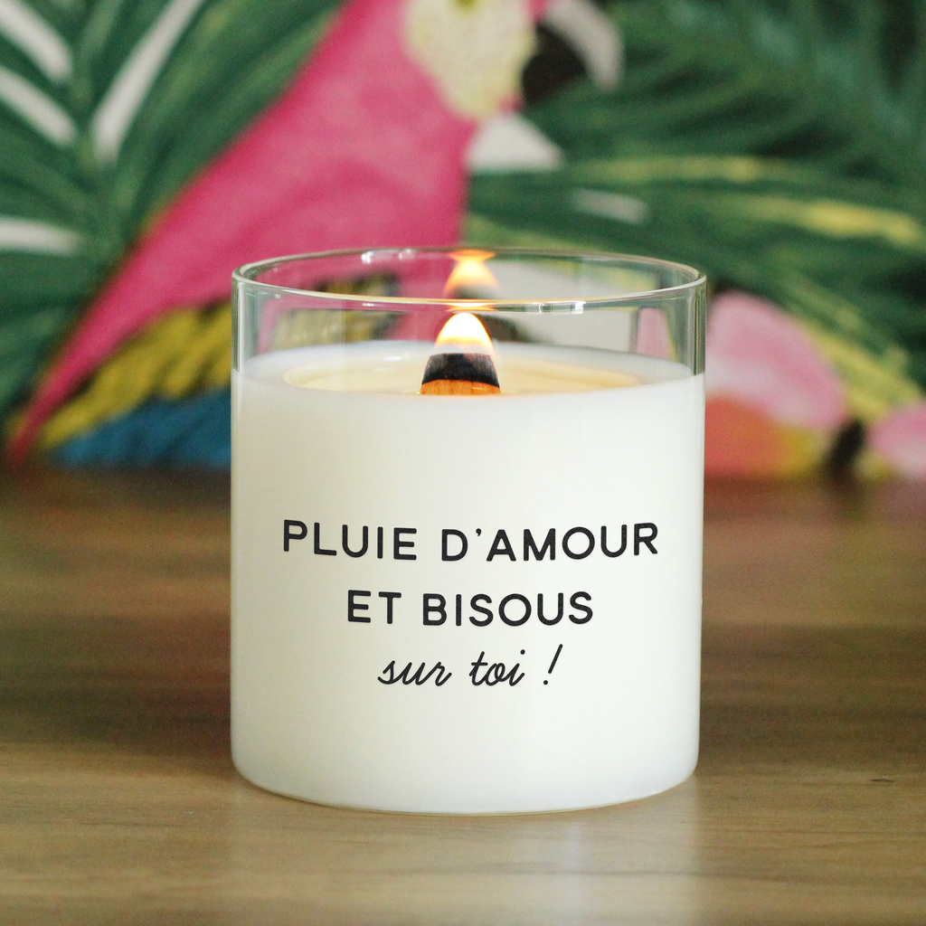 Bougie allumée avec l’inscription "Pluie d’amour et bisous sur toi !", posée sur une table avec un fond tropical coloré, parfaite comme idée cadeau romantique ou attention tendre.