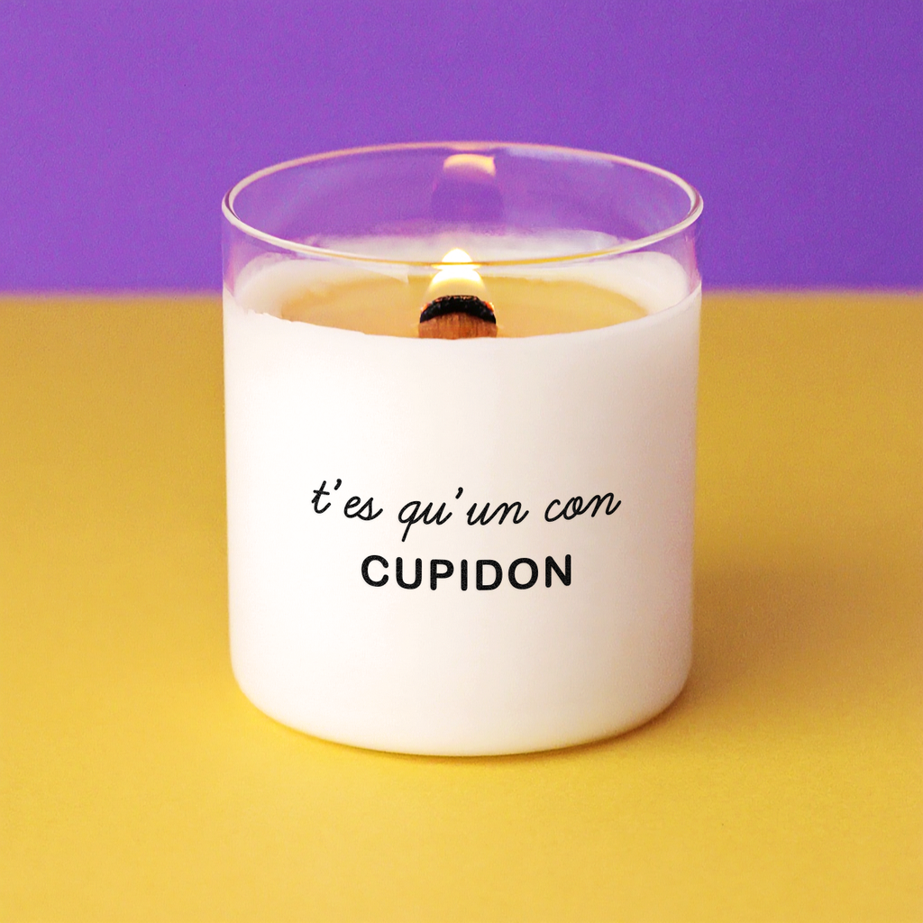 Bougie allumée avec le message "T’es qu’un con, Cupidon", posée sur un fond violet et jaune, parfaite comme idée cadeau sarcastique pour la Saint-Valentin ou après une rupture.