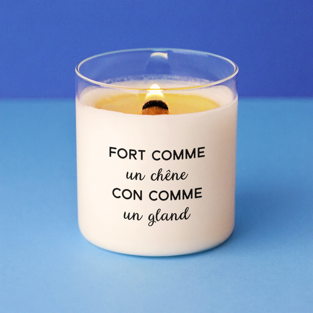 Bougie humoristique allumée avec le message "Fort comme un chêne, con comme un gland", sur fond bleu, parfaite pour un cadeau plein d’ironie et de second degré.