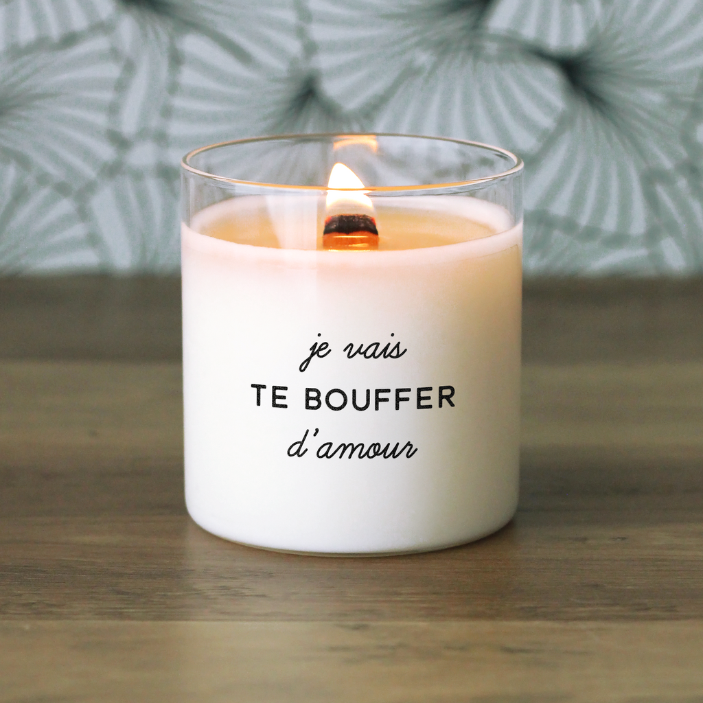Bougie blanche allumée avec le message "je vais te bouffer d’amour", posée sur une table en bois avec un fond graphique vert, idée cadeau originale et passionnée pour couple, amoureux ou crush.