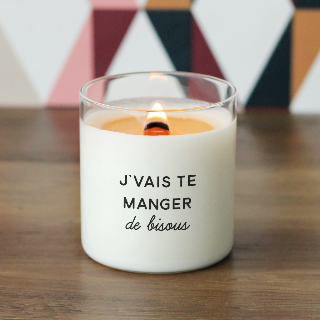 Bougie allumée avec l’inscription "J’vais te manger de bisous", posée sur une table en bois, avec fond graphique coloré, parfaite comme cadeau d’amour ou déclaration affectueuse.
