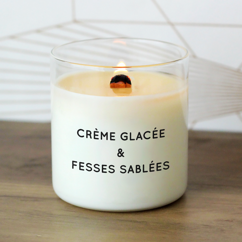 Bougie allumée avec le message "Crème glacée & fesses sablées", posée sur une table en bois, ambiance estivale ensoleillée, parfaite pour offrir à un(e) amateur(trice) d’humour et de plage.