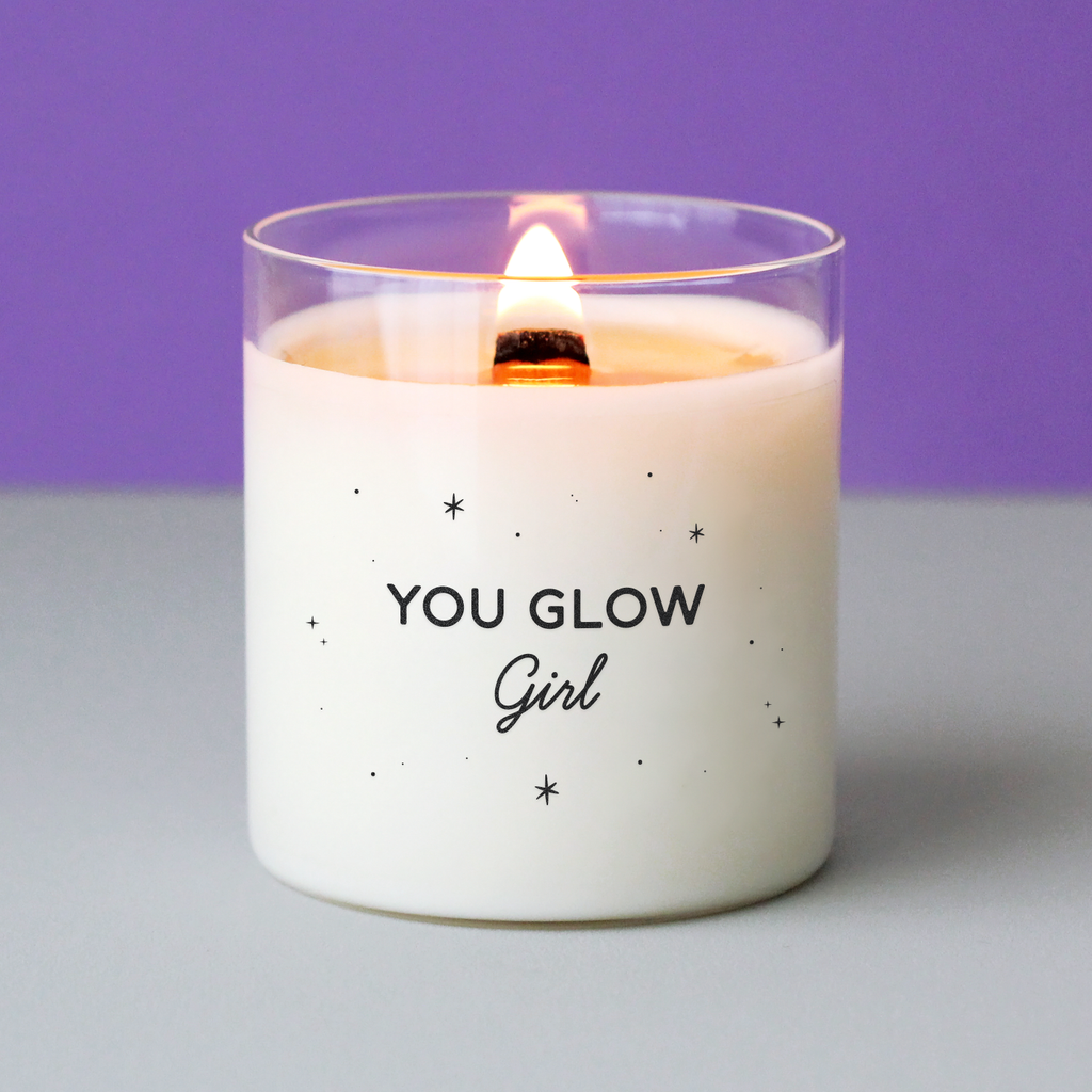 Bougie à message « You glow girl » entourée de petites étoiles noires, imprimée sur cire blanche dans un verre transparent. Idée cadeau lumineuse et inspirante pour une femme rayonnante.