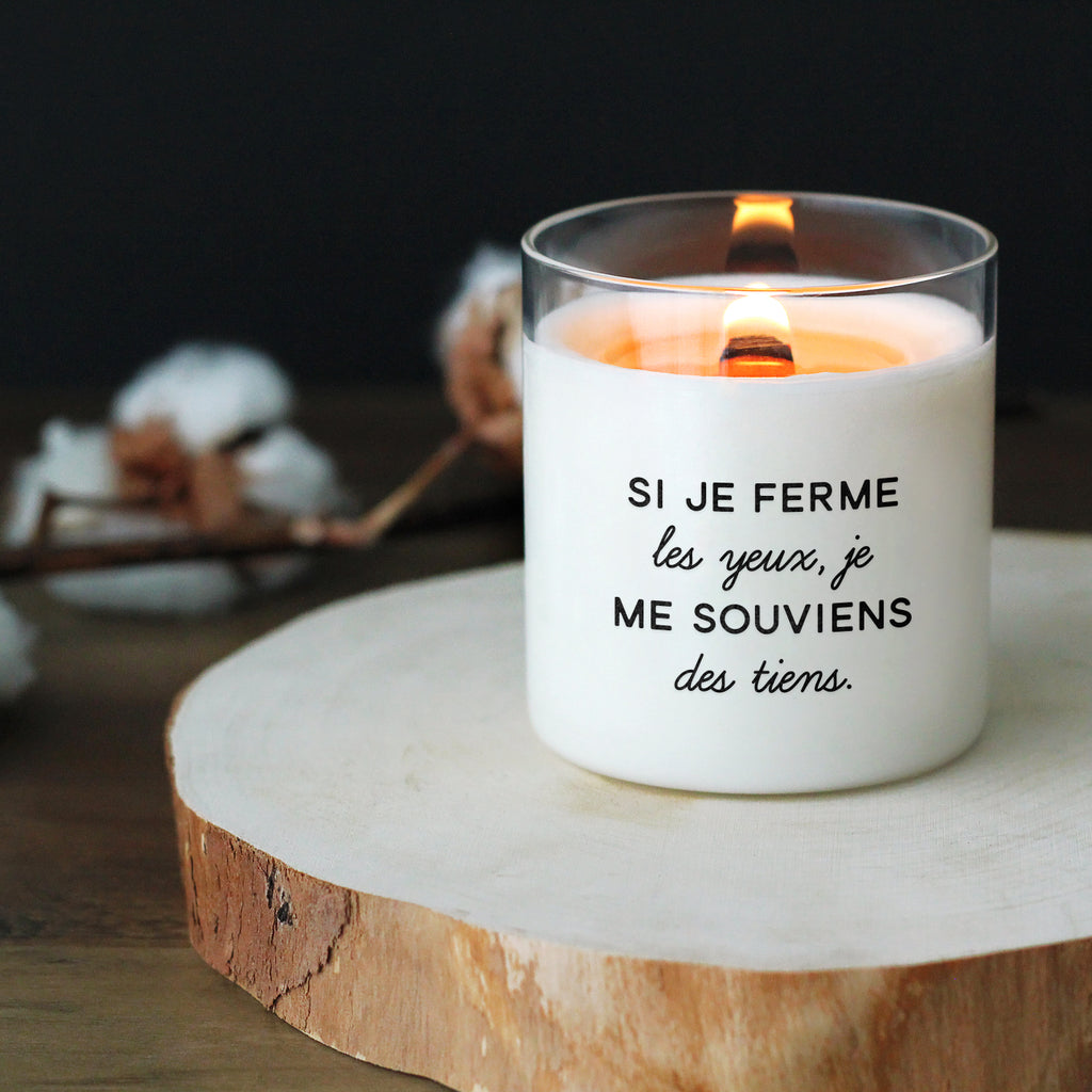 Bougie personnalisée avec le message "Si je ferme les yeux, je me souviens des tiens", allumée sur une planche en bois, avec un fond doux et naturel.